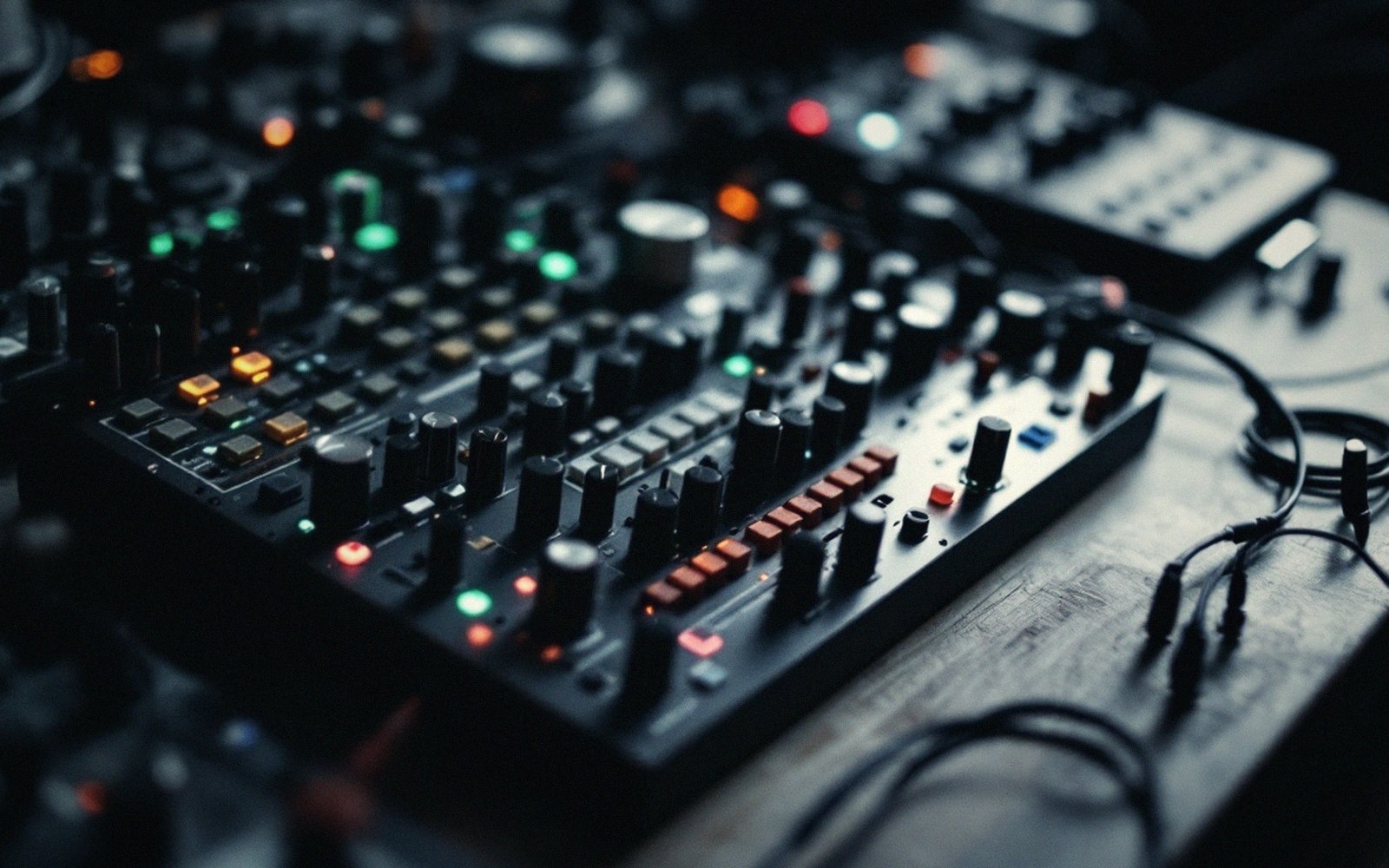 Close-up of a synthesizer mixing console with illuminated knobs, faders and patch cables